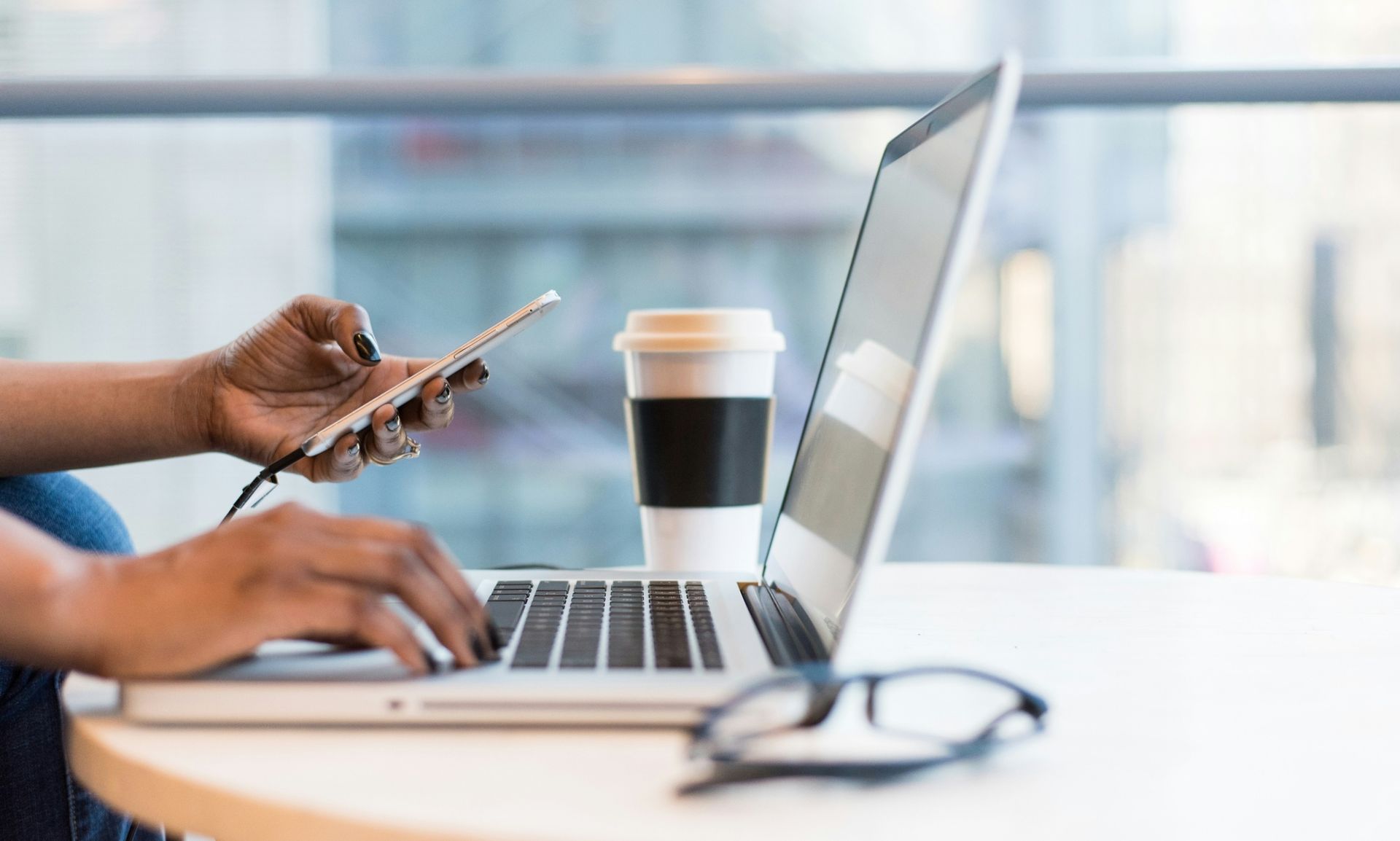 close up of person's hands typing on laptop and holding mobile phone